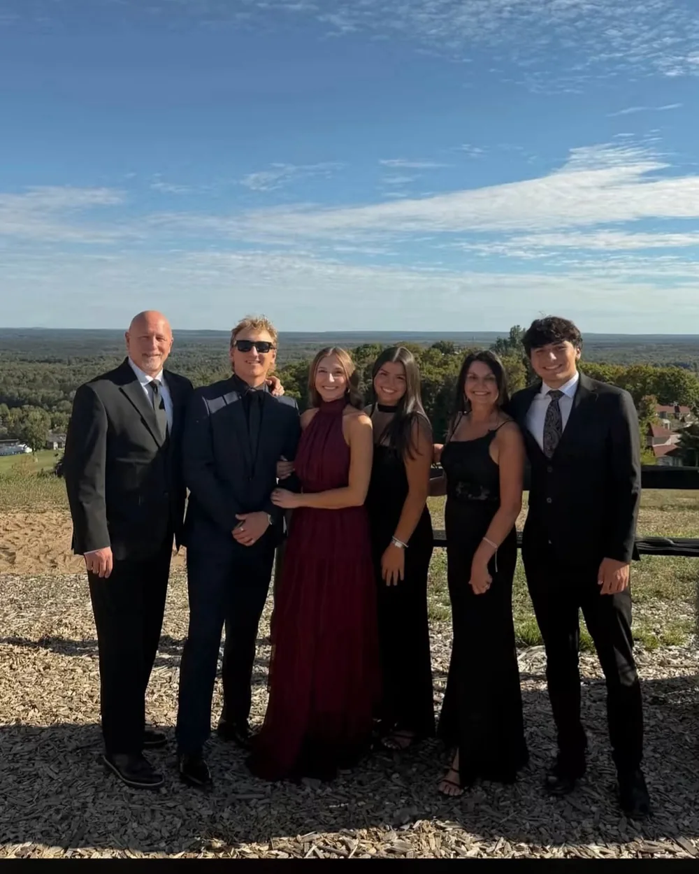 Jay DeBoyer with his family, dressed for a formal celebration outdoors with the Michigan countryside behind them